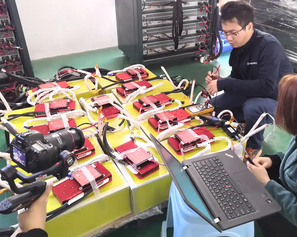 Custom Battery Pack Testing at HiMAXBATT HiMAXBATT engineers testing custom lithium battery packs with BMS boards using a multimeter and laptop