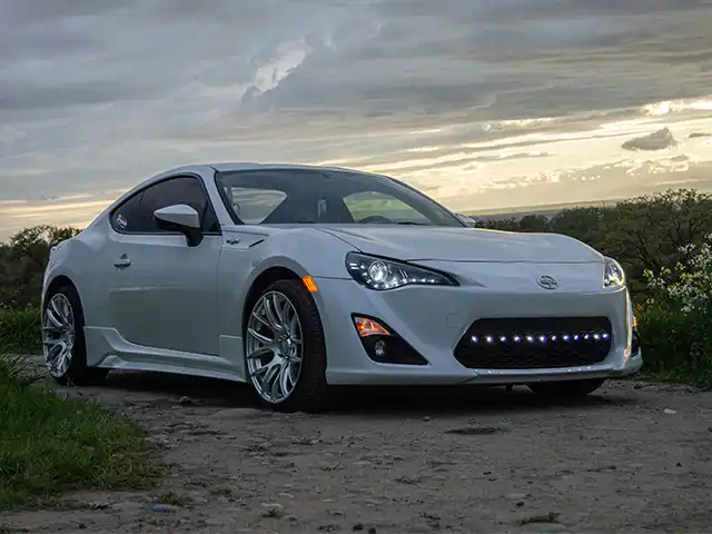 Replacement Battery Packs for Hybrid Cars White coupe parked on a dirt lot at sunset, an application for hybrid car battery pack replacement